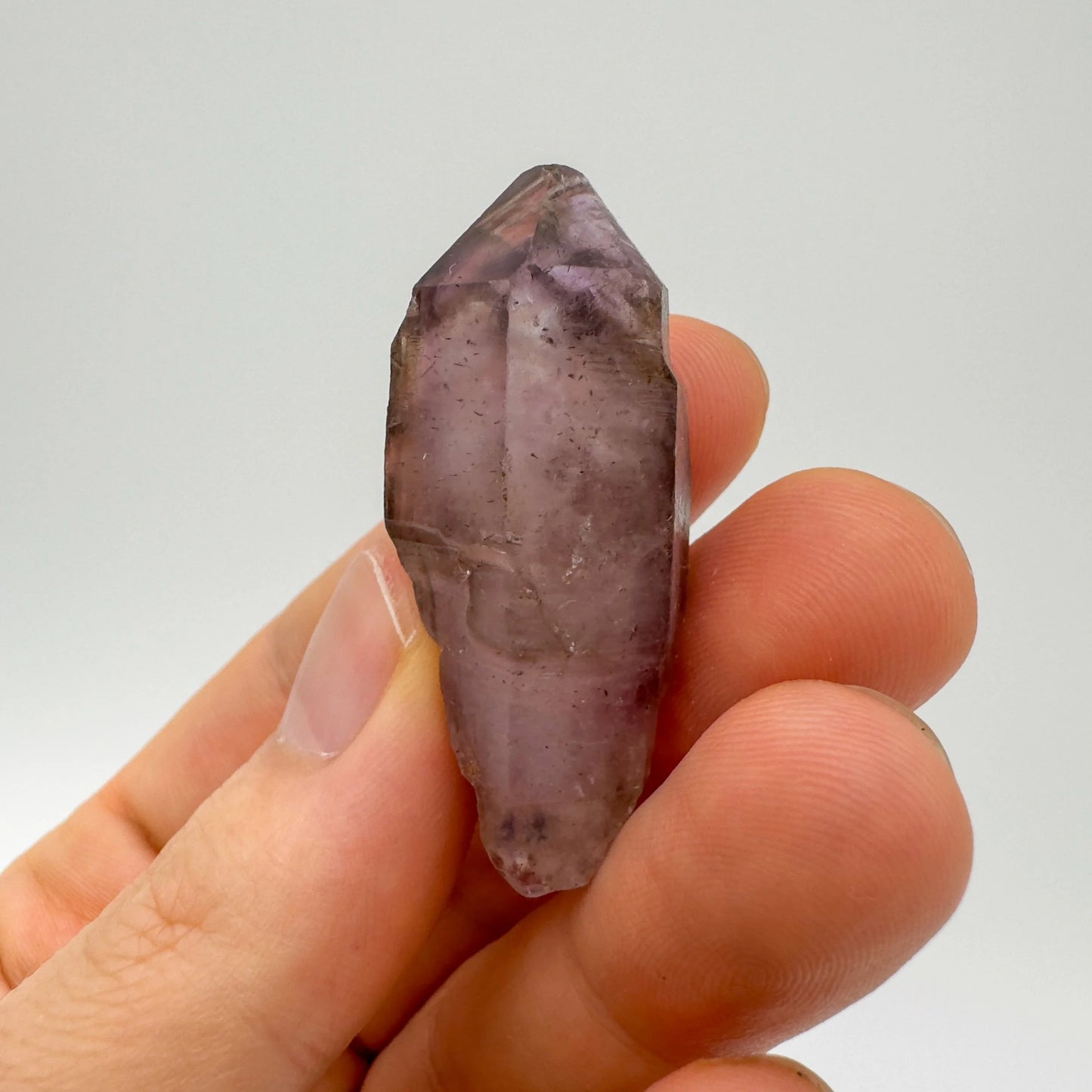 Considered view of Smoky Amethyst raw crystal, from Masvingo, Zimbabwe, shown alongside the hand for scale.
