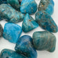 On a soft surface rests an Apatite tumbled stone, from Anosy, Madagascar, traditionally used for Focus, showing the piece in repose.