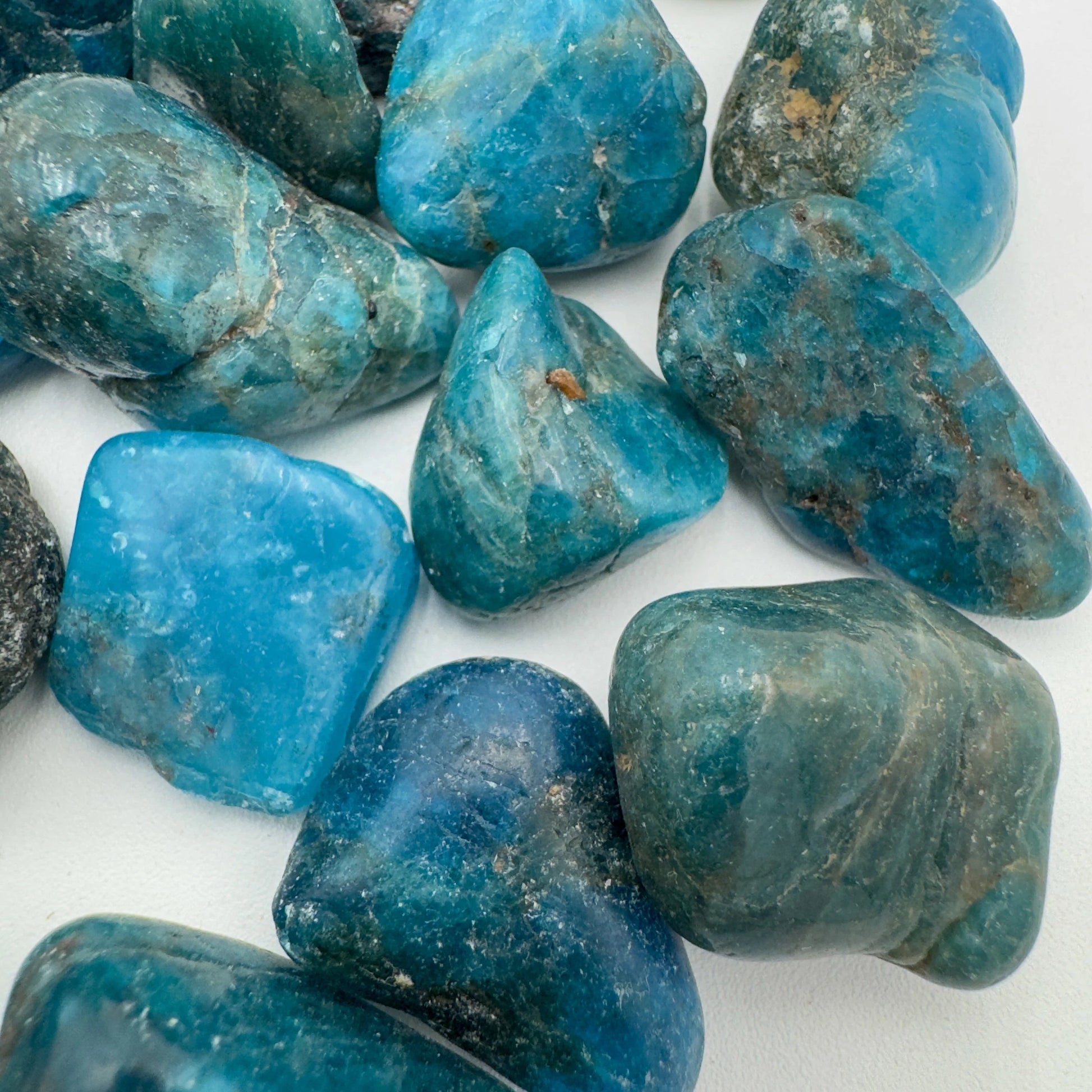 On a soft surface rests an Apatite tumbled stone, from Anosy, Madagascar, traditionally used for Focus, showing the piece in repose.