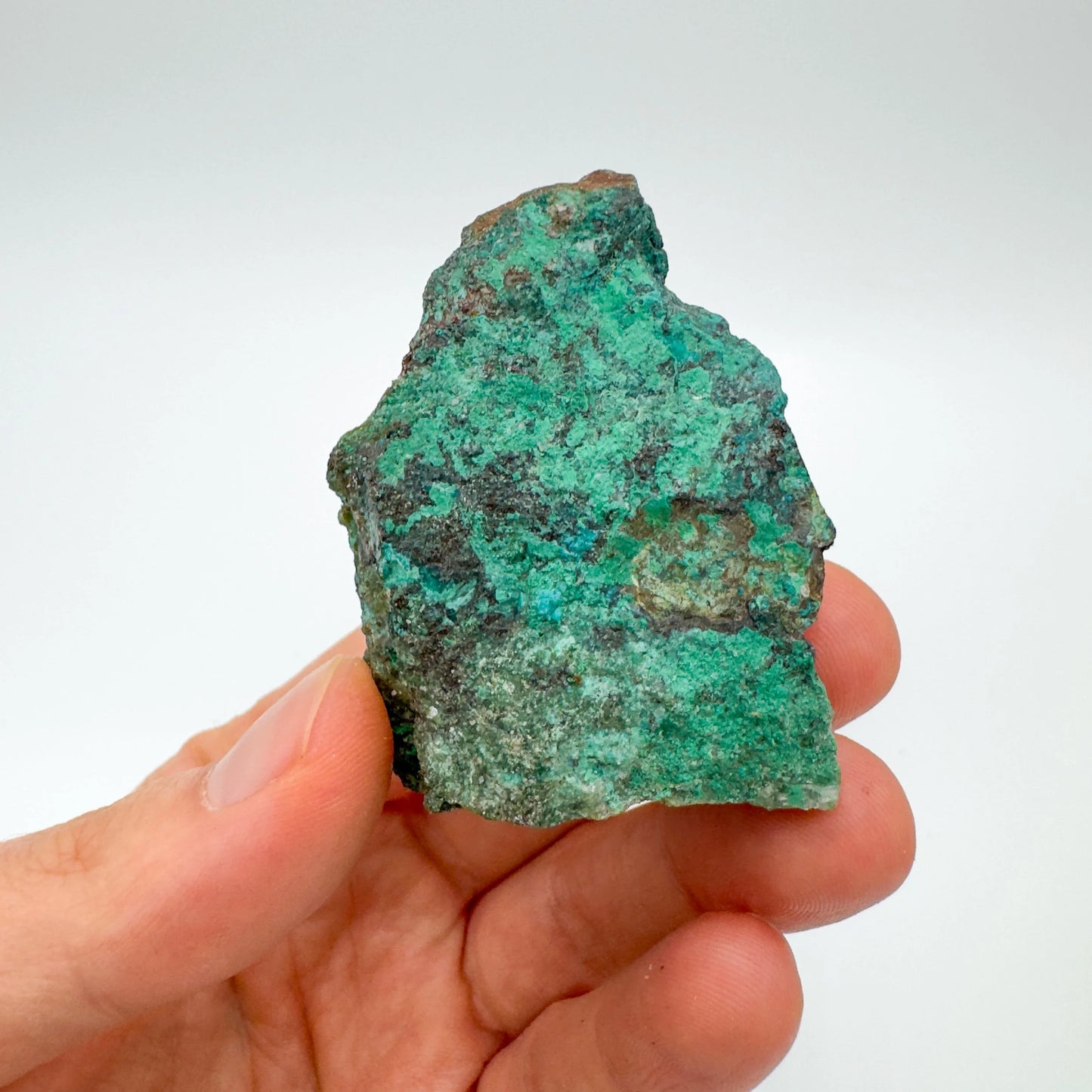 On a soft surface rests a Chrysocolla raw crystal, traditionally used for Emotional Healing, with character of the piece on display.