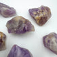 In-hand view of a Amethyst raw stone held against natural backdrop.