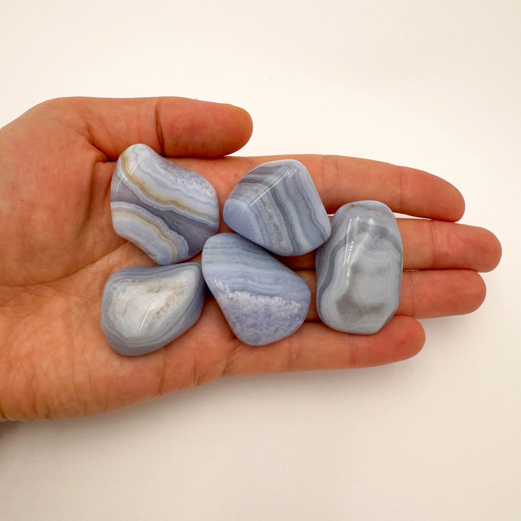 In-hand view of one Blue Lace Agate tumbled stone for scale, sourced from ǁKaras Region, Namibia.