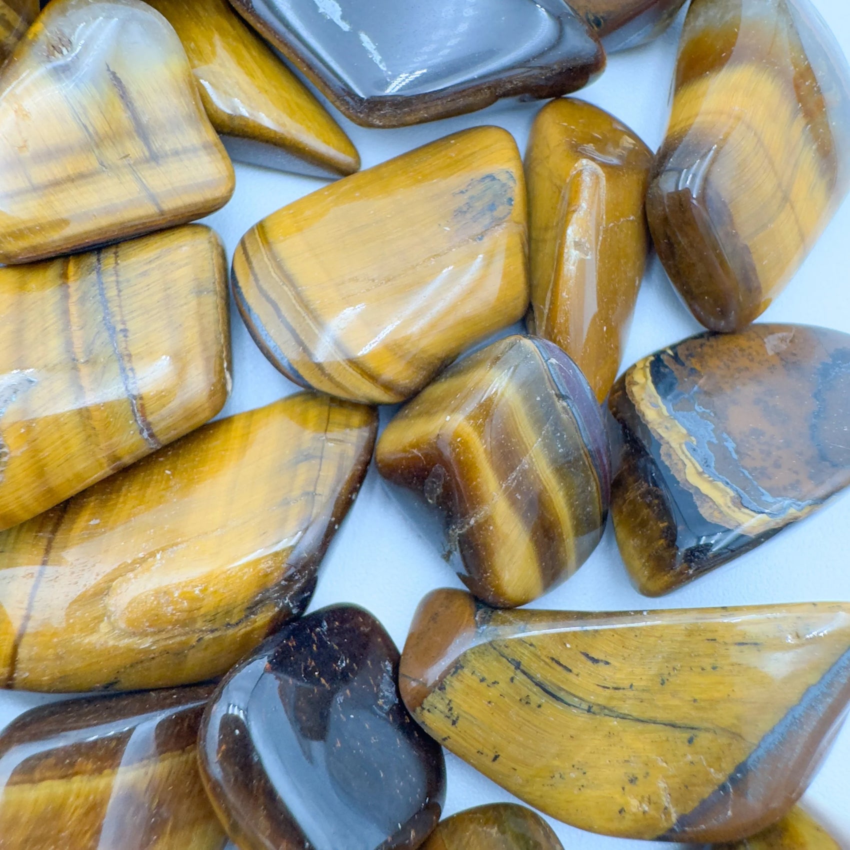 Held in hand, a single Tiger Eye tumbled stone sourced from South Africa.