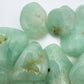 Held in hand, a Prehnite tumbled stone held against natural backdrop.