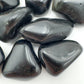 Palm-scale view of a Rainbow Obsidian tumbled stone held against natural backdrop, sourced from Mexico.