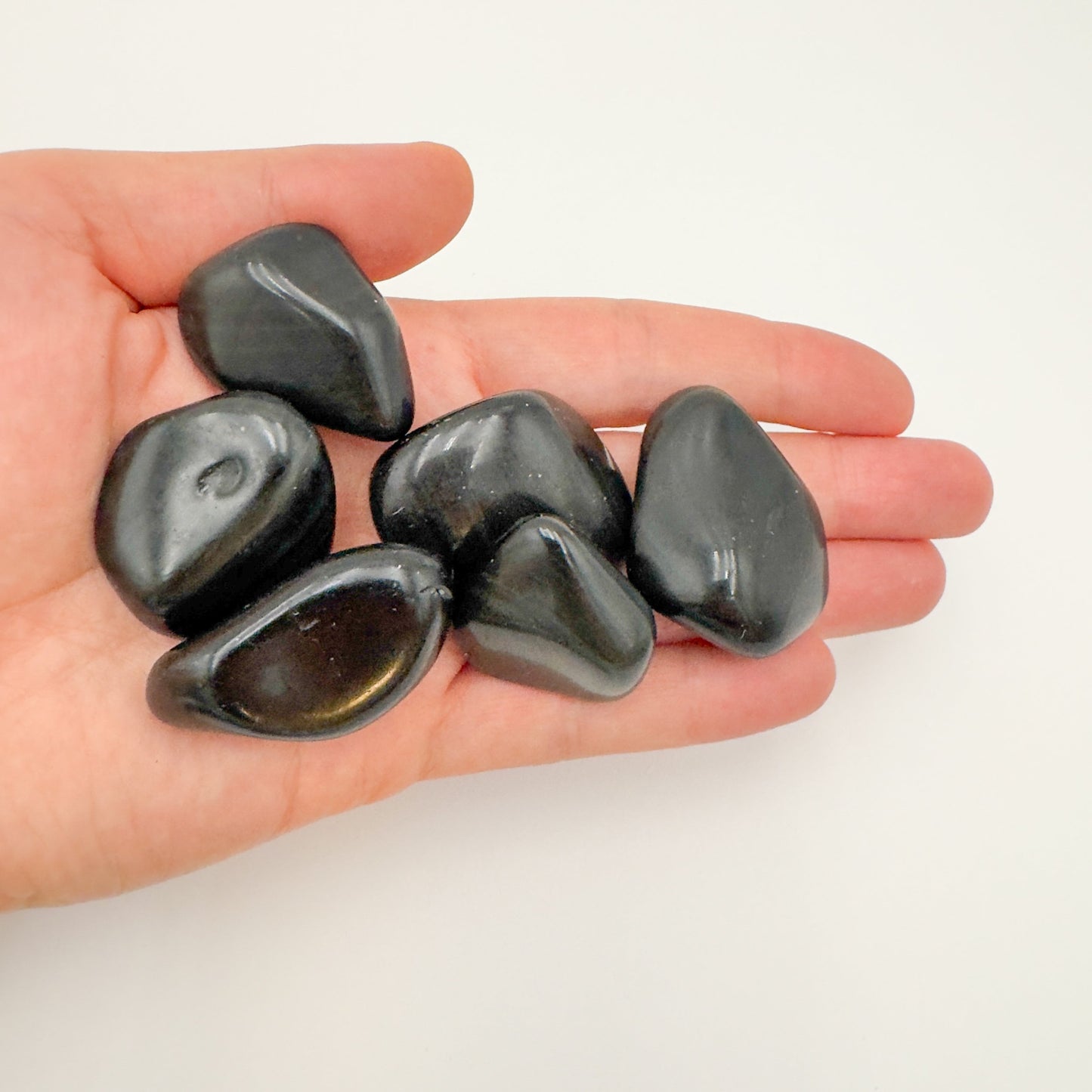 Lifestyle still of Rainbow Obsidian tumbled stone, showing the full body of the piece.