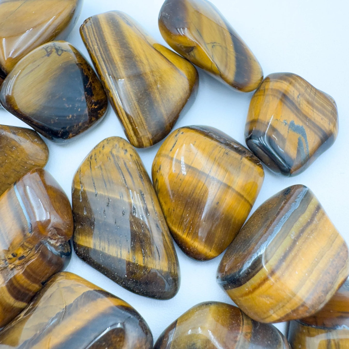 Lifestyle view of a Tiger Eye tumbled stone held against natural backdrop.