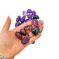 A handful of Ametrine tumbled stones held in an open palm for scale