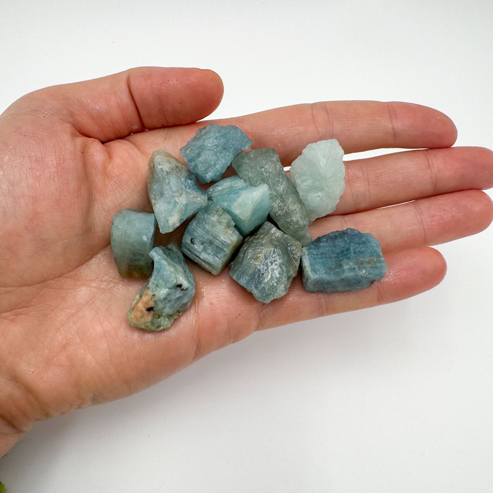 Hand holding small aquamarine raw crystals 5-10 grams Brazil scale reference