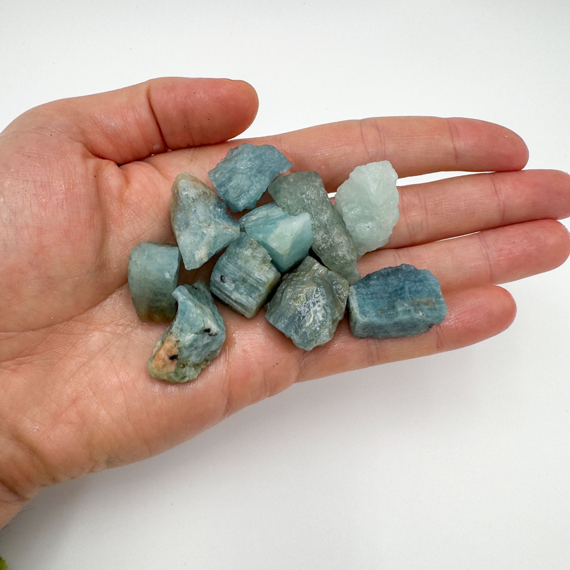 Hand holding small aquamarine raw crystals 5-10 grams Brazil scale reference