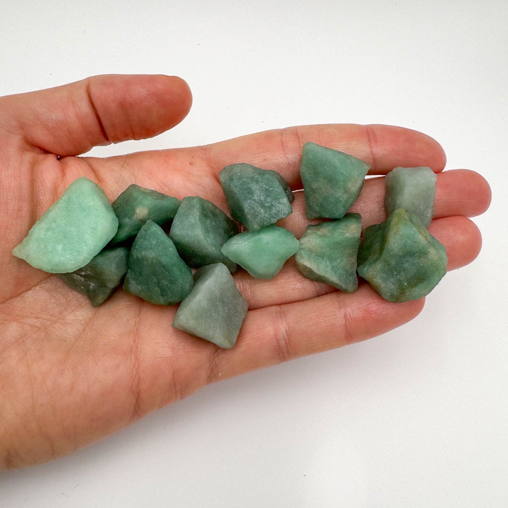 Hand holding small green aventurine raw stones 5-10 grams Brazil scale reference