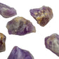 In-hand view of a Amethyst raw stone held against natural backdrop.