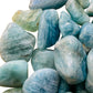 Lifestyle view of a Aquamarine tumbled stone held against natural backdrop, hand-selected from Minas Gerais, Brazil.