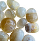 Lifestyle view of a Honey Calcite tumbled stone held against natural backdrop, from Ancash, Peru.