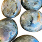 Natural light view of a Labradorite palm stone held against natural backdrop, from Madagascar.