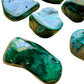 Lifestyle view of a Malachite tumbled stone held against natural backdrop.