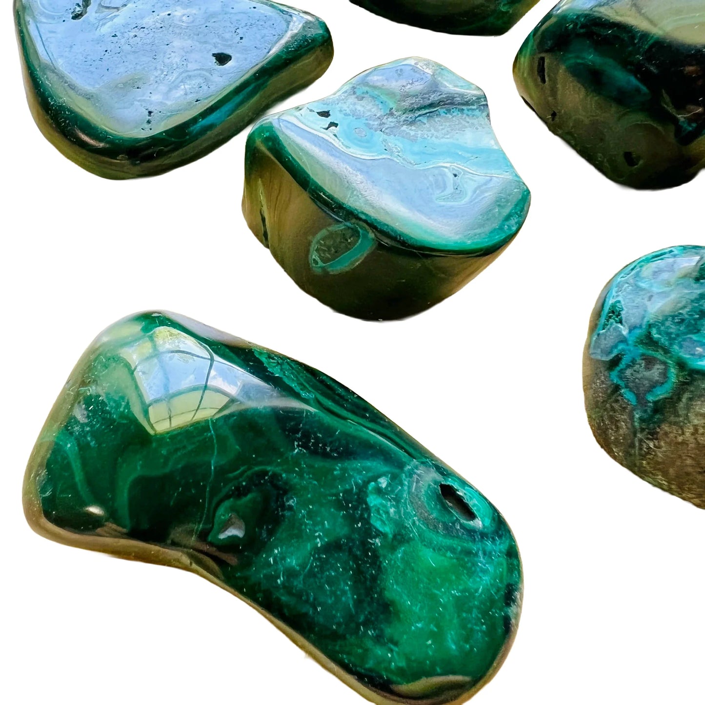 Lifestyle view of a Malachite tumbled stone held against natural backdrop.
