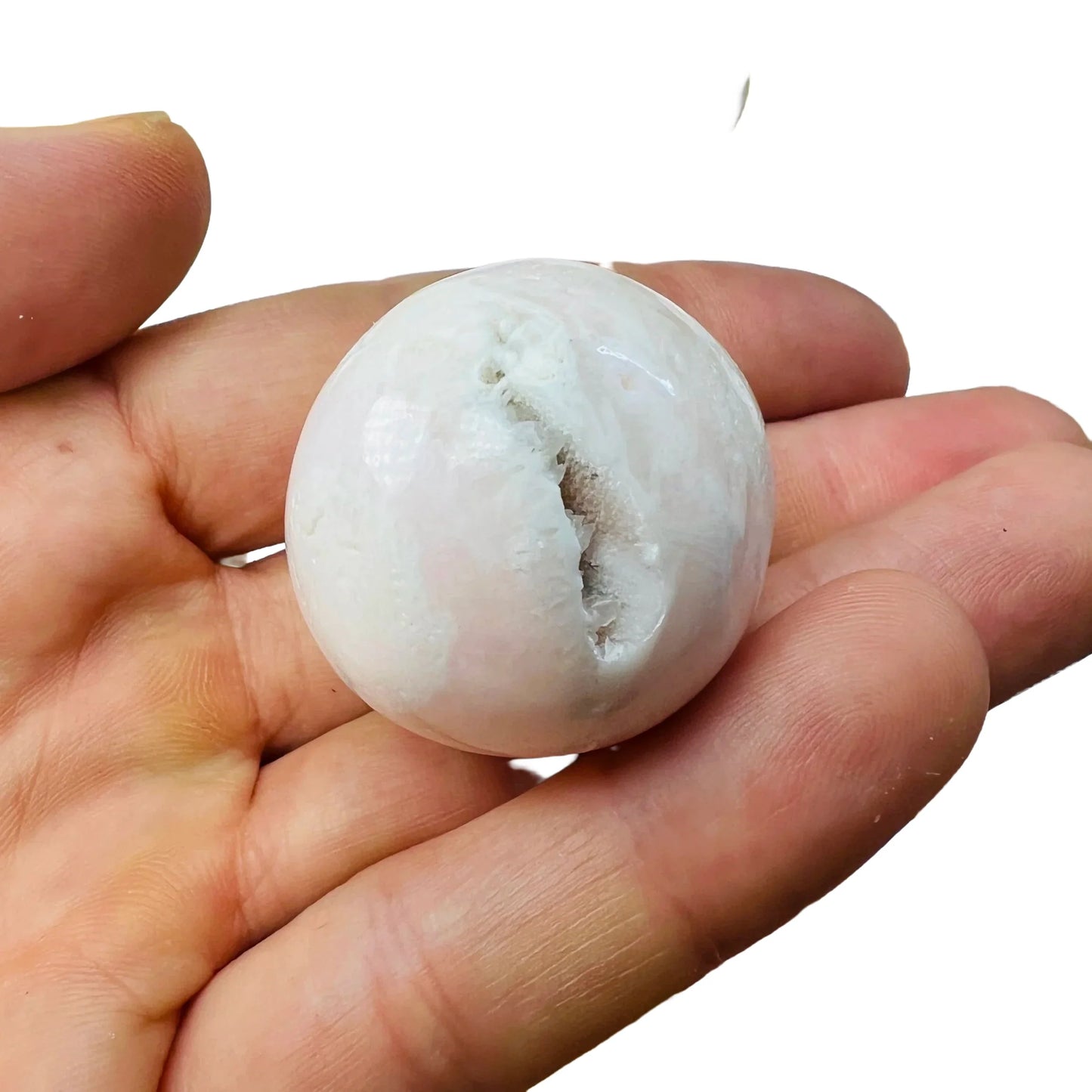 Held against neutral backdrop is a Mangano Calcite tumbled stone, from Ancash, Peru, traditionally used for Stress Relief, showing natural surface character.