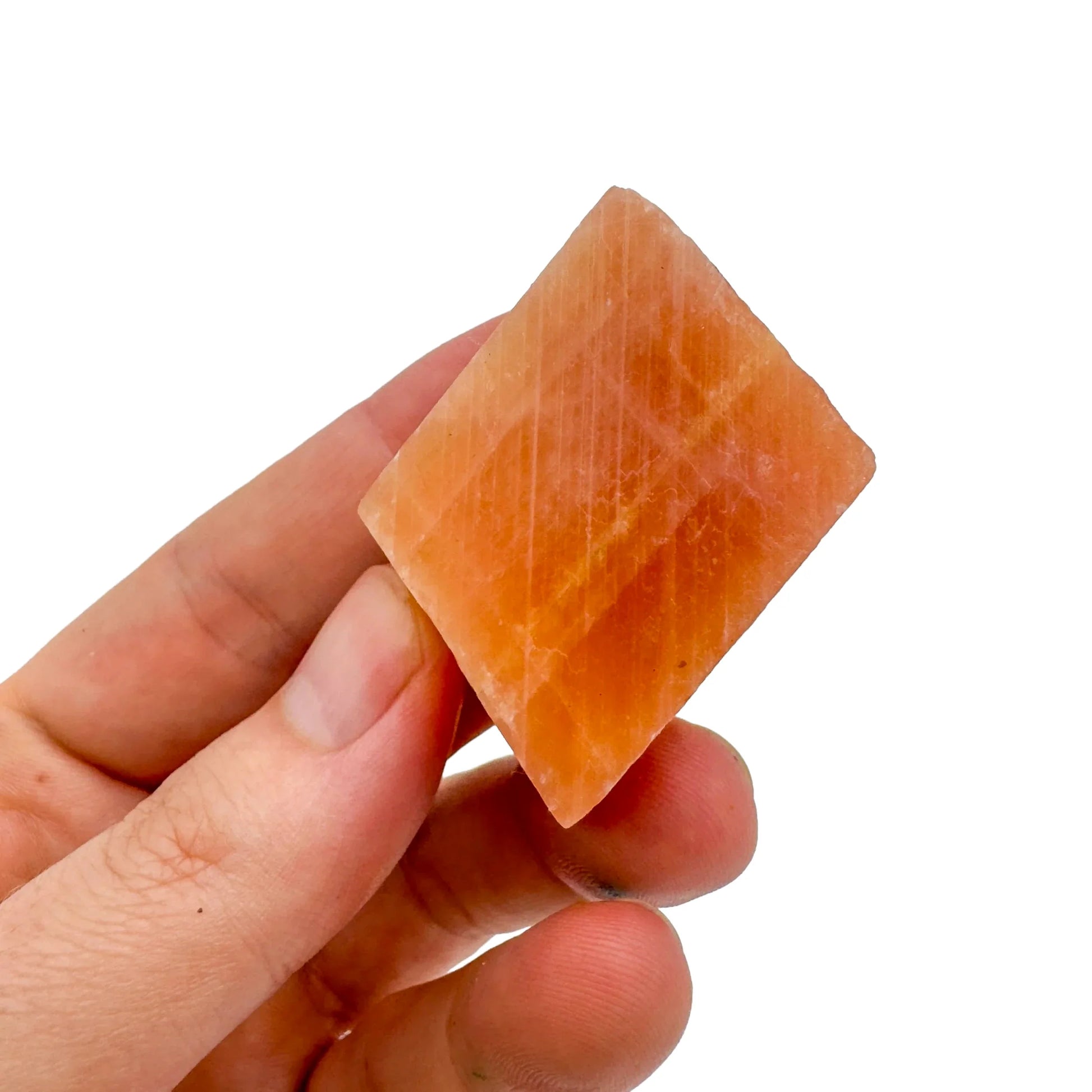 Scale reference of a Orange Calcite raw stone held against natural backdrop.