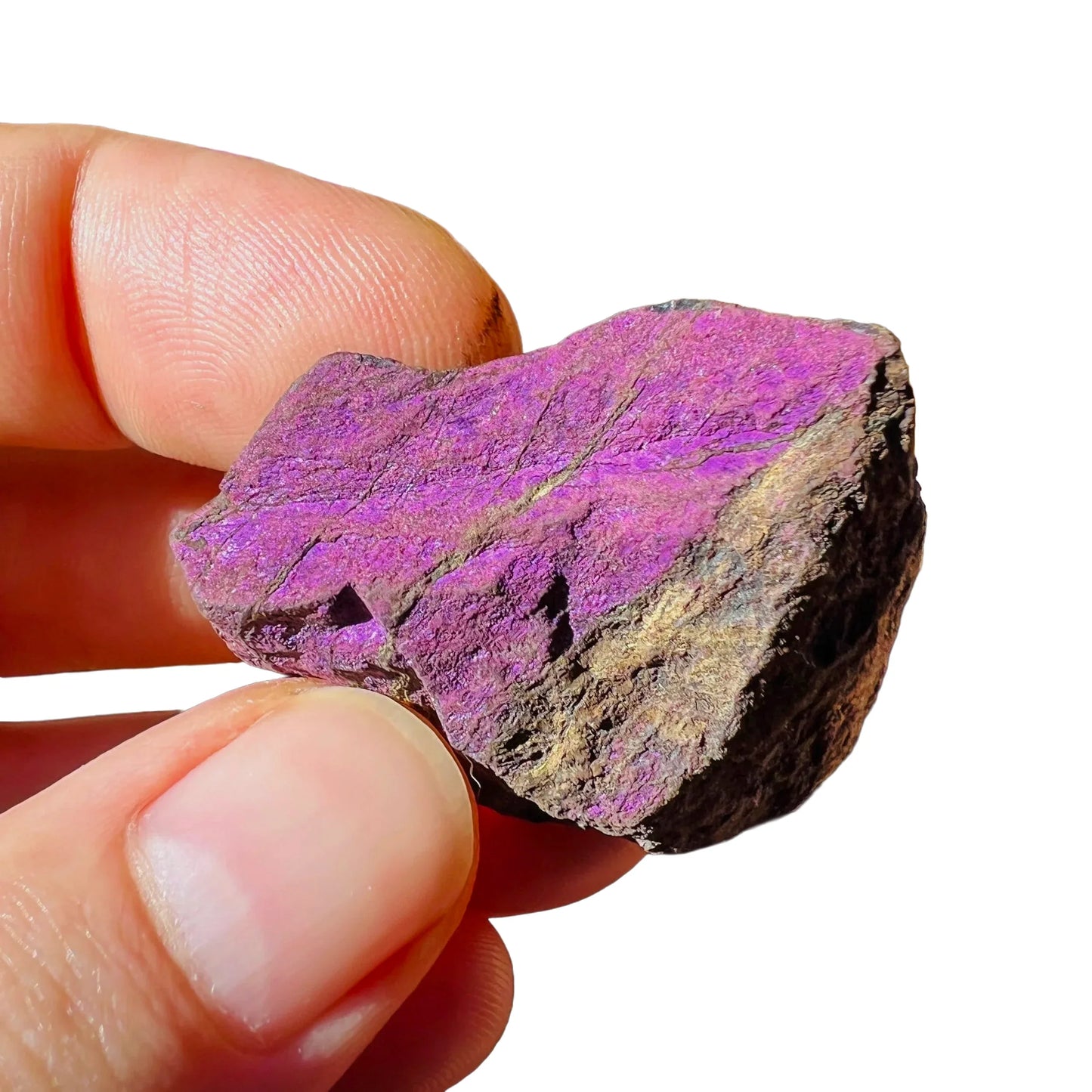 Held against neutral backdrop is a Purpurite raw crystal, associated with Focus, captured in natural daylight.