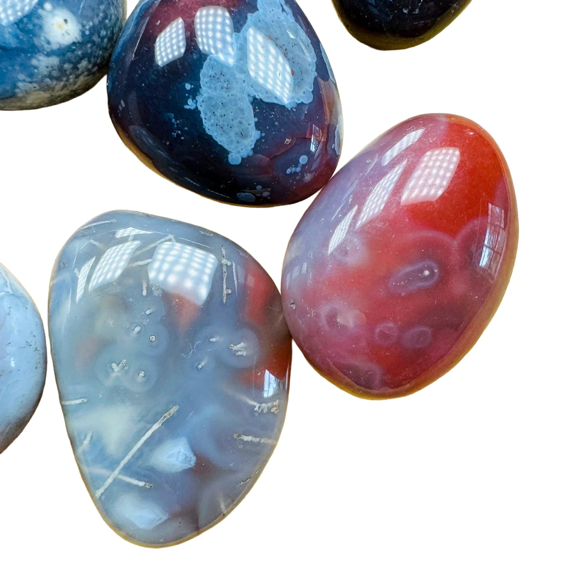 Size comparison with a Red Agate tumbled stone held against natural backdrop.