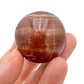 Detail shot of Grade AAA Red Aragonite tumbled stone under natural light