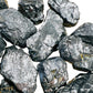Held in hand, a Shungite raw stone held against natural backdrop, from Russia.