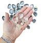 A handful of Clear Quartz tumbled stones held in an open palm for scale