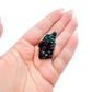 The tiny cube held in a hand, showing the true scale of this 0.68 inch dioptase