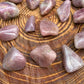 On a soft surface rests a Blue Rose Quartz tumbled stone, associated with Confidence, shown in its everyday setting.