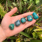 Held in hand is a Chrysocolla tumbled stone, from Arequipa, Peru, showing the piece in repose.