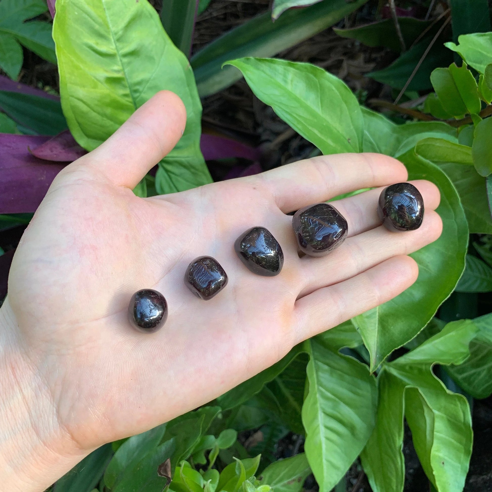 In-hand view of a Garnet tumbled stone, hand-selected from Minas Gerais, Brazil.