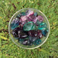 Natural light view of a Fluorite tumbled stone held against natural backdrop.