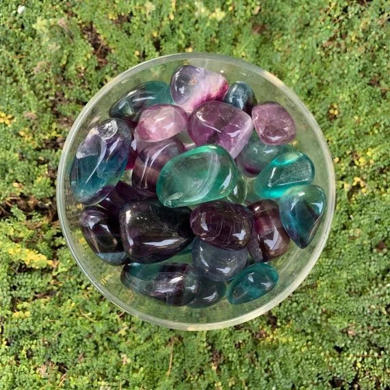 Natural light view of a Fluorite tumbled stone held against natural backdrop.