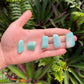 Held against neutral backdrop is an Amazonite tumbled stone, with subtle natural color showing through.