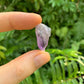 Lifestyle view of a Amethyst raw stone held against natural backdrop.
