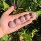 Hand-held view of a single Rhodonite tumbled stone Peru-sourced, sourced from Peru.