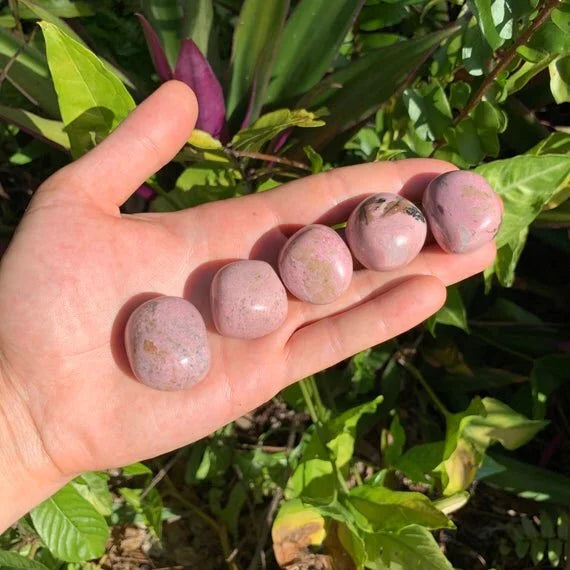 Hand-held view of a single Rhodonite tumbled stone Peru-sourced, sourced from Peru.