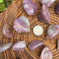Hand-scale shot of a Blue Rose Quartz tumbled stone held against natural backdrop, sourced from Alaotra-Mangoro, Madagascar.