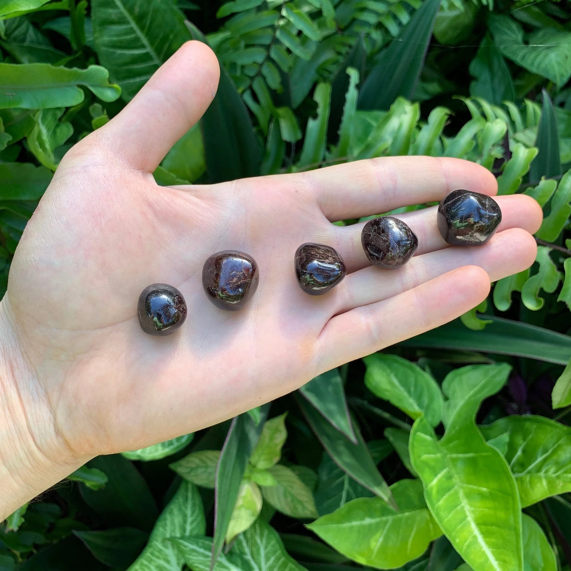 Held in palm of a Garnet tumbled stone, from Minas Gerais, Brazil, associated with Energy, with surface texture in view.