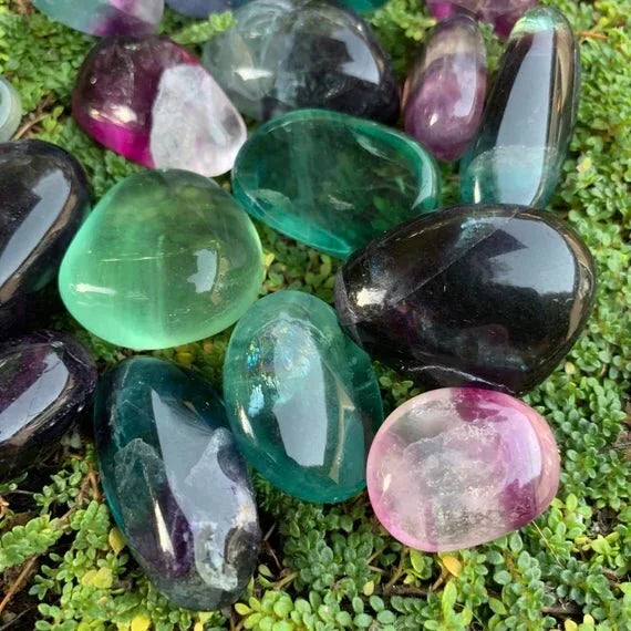 Held against neutral backdrop is a Fluorite tumbled stone, with subtle natural color showing through.