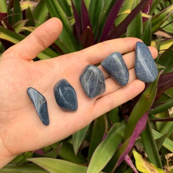 Held in hand, a Lazulite tumbled stone held against natural backdrop, hand-selected from Amoron'i Mania, Madagascar.