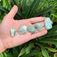 Held in hand is a Chrysoprase tumbled stone, from Bahia, Brazil, with character of the piece on display.