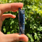 Daylight view of a Blue Kyanite raw stone held against natural backdrop.