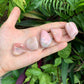 Scale reference of a Pink Opal tumbled stone held against natural backdrop, Peru-sourced.