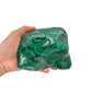Malachite specimen held in hand for scale, showing the stone spans roughly 5 by 4 inches across its widest face.