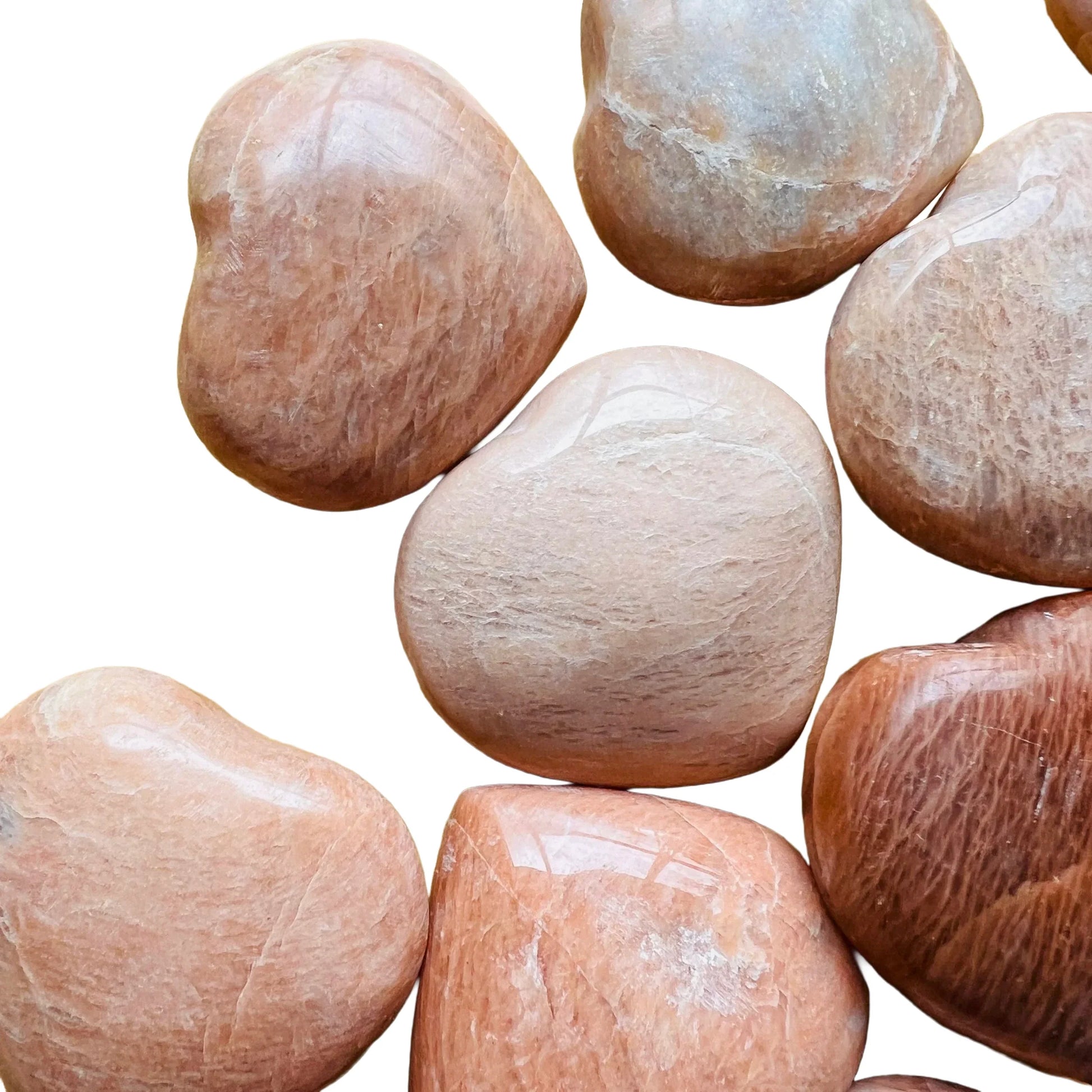 In-hand view of a Peach Moonstone polished heart held against natural backdrop.