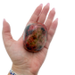 Rhodonite polished free form from Zimbabwe held in hand to show scale