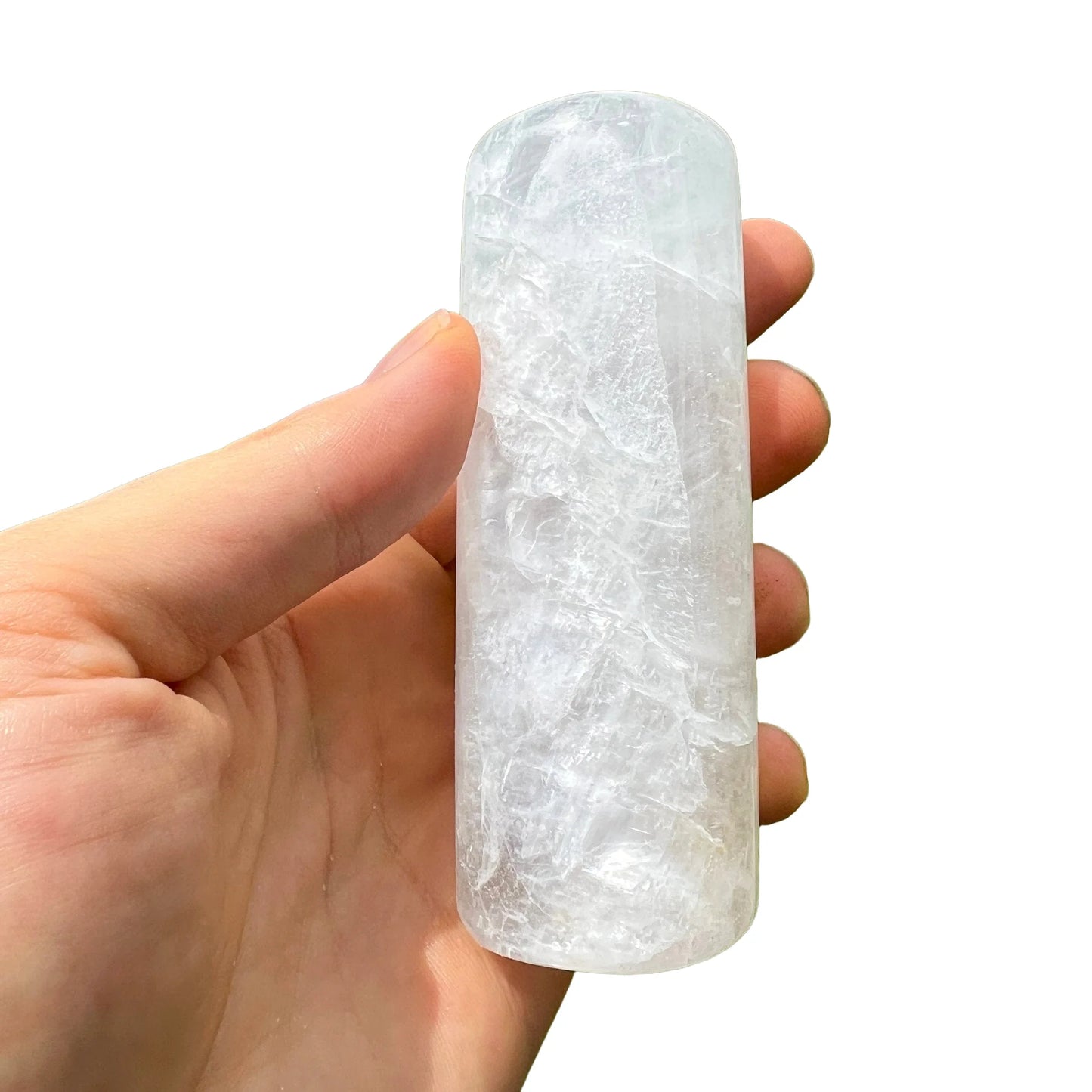 Hand-held view of a Selenite polished cylinder held against natural backdrop.