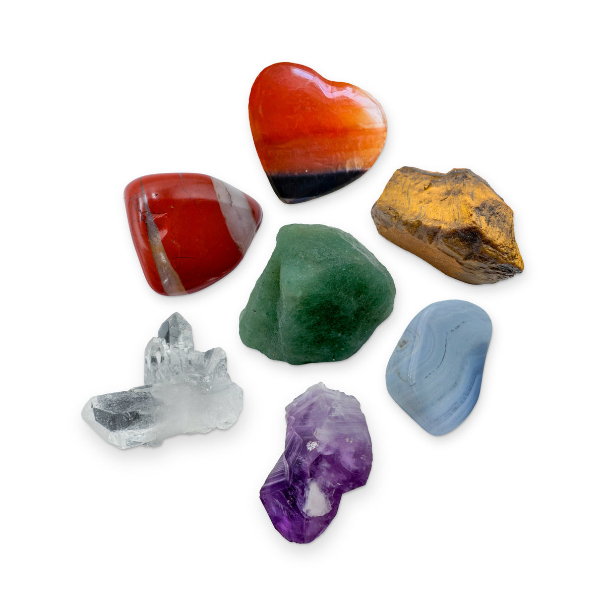 The Seven Chakra Kit: red jasper, carnelian heart, tiger eye, green aventurine, blue lace agate, amethyst point and clear quartz cluster, shown together on white